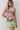 A woman modeling a sleeveless mini dress with an abstract, painterly print featuring a football scene in green, red, blue, and white.