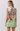 A woman shown from the back wearing a sleeveless mini dress with a large open back and tie detail, featuring an abstract multicolor painting print with green, blue, red, and white tones.