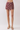 A model's lower body wearing a pair of high-waisted, short wrap-style shorts with a maroon and gold paisley pattern, paired with beige heeled sandals against a light gray studio background.
