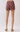 A person shown from the back wearing patterned shorts in burgundy with a multicolor paisley print, paired with beige block-heel mule sandals against a light gray studio background.