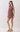 A woman modeling a sleeveless peplum romper with a burgundy and beige paisley pattern, paired with beige block-heel sandals, against a plain light gray studio background.