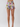 A model's lower body wearing high-waisted, ruffled shorts with a colorful floral and butterfly print on a light beige background, photographed against a neutral light gray studio backdrop.