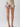 A person from the waist down wearing floral print shorts with a ruffled hem and beige strappy sandals, photographed against a light gray studio background.