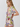 A woman wearing a short-sleeve tropical floral print romper with a tie-front neckline and ruffled edges, photographed against a plain light gray studio background.