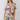 A woman modeling a short-sleeve floral romper with a tie-front neckline and ruffled edges, photographed against a plain light gray studio background.