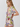 A woman wearing a short-sleeve wrap dress with a colorful tropical floral print on a light beige background, photographed against a plain light gray studio backdrop.