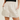 A close-up of a model wearing light beige faux-leather shorts with an elastic waistband and side pockets, paired with a black top against a light beige background.