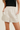 A close-up of a model wearing light beige faux-leather shorts with an elastic waistband and side pockets, paired with a black top against a light beige background.