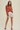 A woman modeling a rust-colored knit sweater and light beige shorts against a solid light beige background.