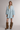 A model wearing a light blue denim shirt dress with long bell sleeves and brown suede fringe boots, standing against a neutral studio background.