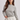 A woman wearing a gray and white horizontally striped long-sleeve knit top with white drawstring pants, photographed against a light gray studio background.