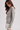 A woman wearing a gray and white horizontally striped long-sleeve knit top, paired with a white skirt, photographed against a light gray studio background.