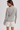 A woman shown from the back wearing a gray and white horizontally striped long-sleeve top and white shorts with a scalloped lace hem, set against a plain light gray studio background.
