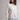 A woman wearing a cream and light blue striped long-sleeve mock neck top and light blue textured pants, standing against a neutral light gray studio background.