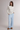 A woman modeling a cream ribbed long-sleeve mock neck top and light blue wide-leg pants, paired with brown slippers, against a neutral light gray studio background.