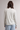 A woman shown from the back wearing a cream-colored long-sleeve top with thin light blue horizontal stripes and light blue ribbed pants, set against a plain light gray studio background.