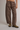 A person wearing wide-leg brown drawstring pants with large front patch pockets and olive green lace-up boots, photographed against a plain light gray studio background.