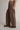 A person wearing wide-leg brown pants with an elastic waistband and drawstring, paired with olive green work boots, shown from the waist down against a plain light gray studio background.