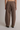 A person shown from the back wearing loose, wide-leg brown pants with an elastic waistband and two back patch pockets, photographed against a plain light gray studio background.