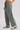 A person wearing wide-leg sage green pants with an elastic drawstring waist and side pockets, paired with white sneakers, shown from the waist down on a light gray studio background.