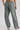 A person shown from the back wearing loose, wide-leg sage green pants with an elastic waistband and two large back patch pockets, paired with white sneakers with black stripes.