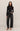 Woman wearing a black long-sleeve top and black jeans on a plain background