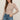 Woman wearing a beige knitted sweater and blue jeans against a plain background