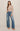 Woman wearing a beige sweater and blue jeans on a plain background