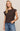 Woman wearing a brown top with unique shoulder designs against a beige background