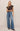 Woman wearing a brown top and blue jeans against a beige background
