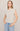 Woman wearing a beige sleeveless top with button details and light blue jeans on a plain background