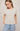 Woman wearing a beige top with button details and light blue jeans on a plain background