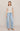 Woman wearing a beige top with decorative sleeves and light blue jeans on a plain background