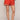 Person wearing red shorts with white floral embroidery on a plain background