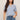 Woman wearing a light blue cable knit top and jeans on a beige background