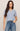 Woman wearing a light blue cable knit top and jeans on a beige background