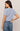 Woman wearing a light blue textured top and jeans on a beige background
