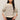 A woman modeling a cream-colored knit sweater with horizontal black and gray stripes, paired with black jeans, against a plain light beige studio background.