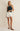 Woman wearing a navy sleeveless top and white shorts on a beige background