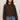 Woman wearing a brown sweater and blue jeans against a plain background
