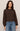 Woman wearing a brown sweater and blue jeans against a plain background