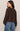 Woman wearing a brown sweater and blue jeans against a beige background