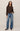 A woman modeling a dark brown long-sleeve knit sweater and wide-leg blue jeans against a plain light beige studio background.