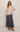 A model wearing a beige knit V-neck sweater and a navy blue plaid midi skirt, paired with brown suede ankle boots and dark sunglasses, against a plain light beige studio background.