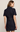 A woman shown from the back wearing a dark indigo denim short-sleeve dress with a collar and a matching belt at the waist, set against a plain light beige studio background.