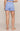 A person shown from the back wearing light blue ribbed shorts and a matching cropped top against a plain beige studio background.