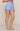 A model wearing light blue textured shorts with a scalloped hem, shown from the waist down against a plain beige studio background.