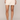 A model wearing a cream-colored mini skirt with floral lace trim along the hem, paired with nude high-heeled sandals against a light beige studio background.