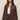 Woman wearing a brown suede jacket over a white top and brown shorts on a beige background