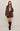 Woman wearing a brown textured jacket and skirt with black knee-high boots on a plain background